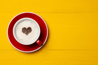 Cup of aromatic coffee with heart shaped decoration on yellow wooden table, top view. Space for text