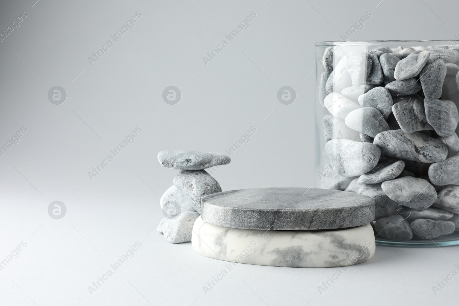 Photo of Presentation for product. Podium and glass container with stones on light grey background. Space for text