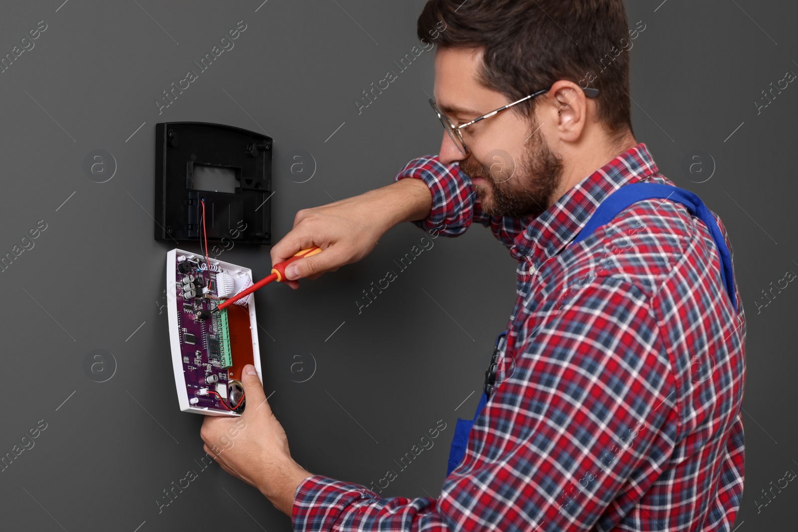 Photo of Technician installing home security alarm system on gray wall indoors