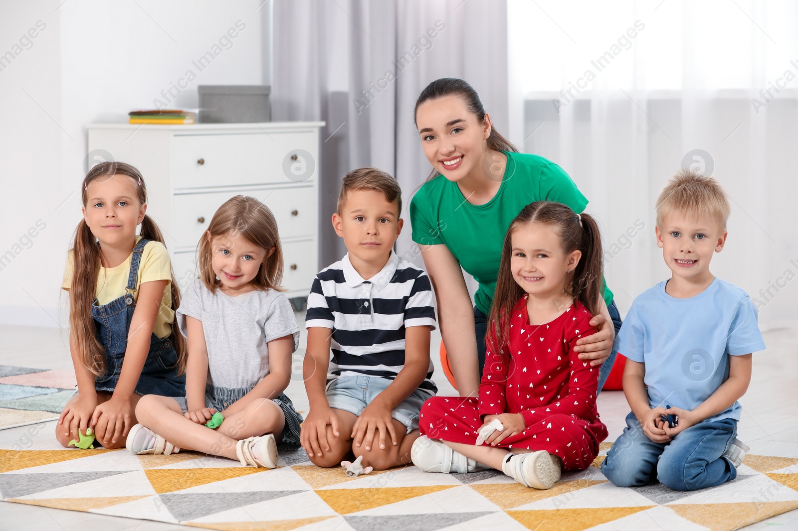 Photo of Nursery teacher and group of cute little children on floor in kindergarten. Playtime activities