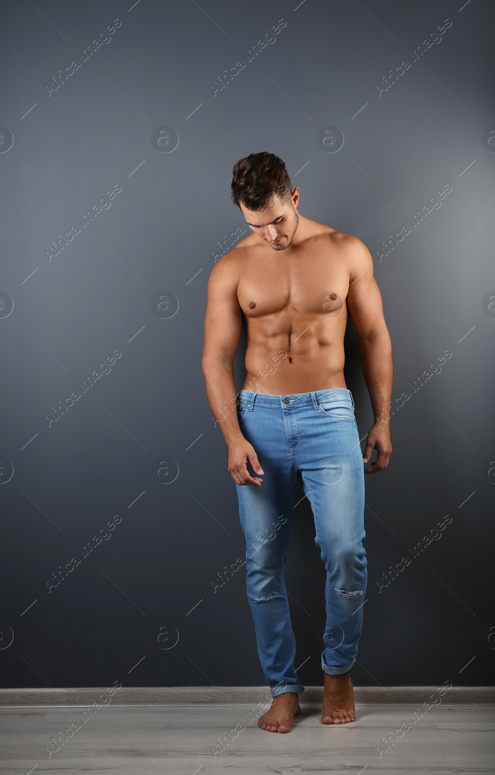 Photo of Shirtless young man in stylish jeans near grey wall