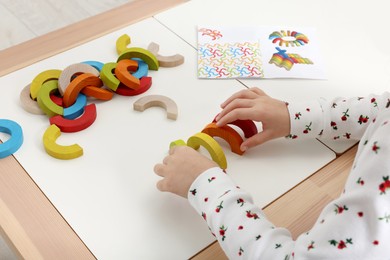 Photo of Motor skills development. Girl playing with colorful wooden arcs at white table indoors, closeup