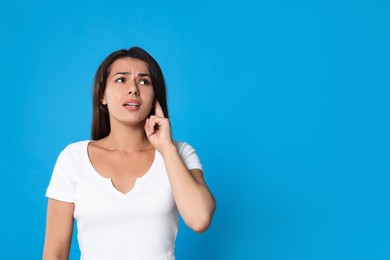 Photo of Young woman suffering from ear pain on light blue background, space for text