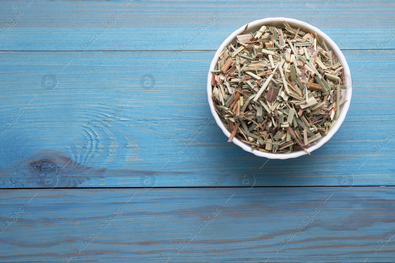 Photo of Bowl with aromatic dried lemongrass on light blue wooden table, top view. Space for text