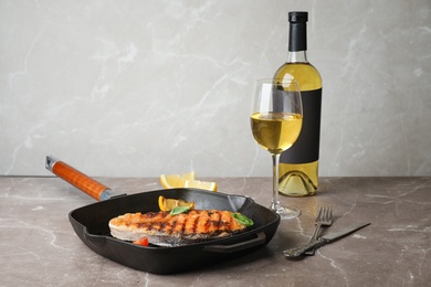 Frying pan with tasty salmon steak and wine on table