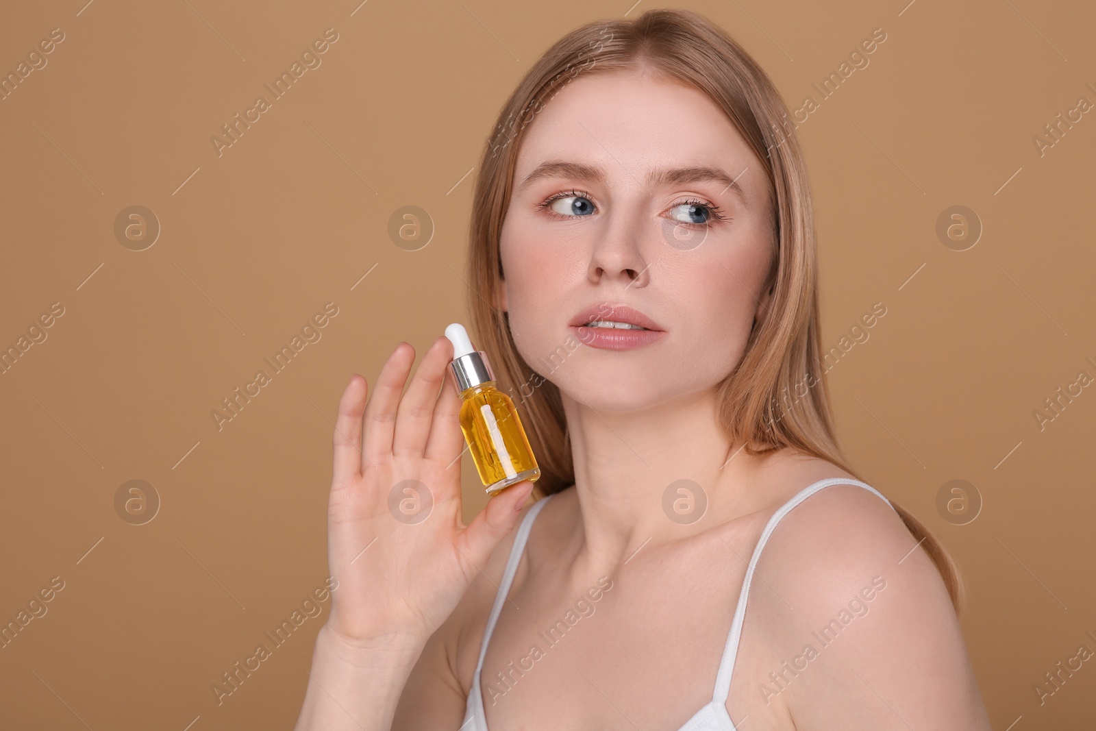 Photo of Beautiful young woman with bottle of essential oil on brown background