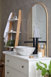 Photo of Stone vessel sink with faucet and toiletries on white countertop in bathroom