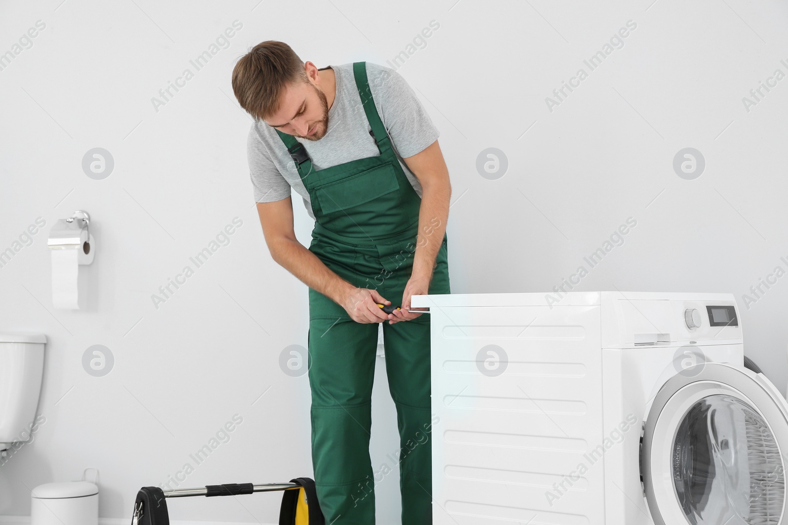 Photo of Young plumber fixing washing machine in bathroom