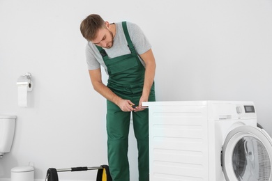 Young plumber fixing washing machine in bathroom