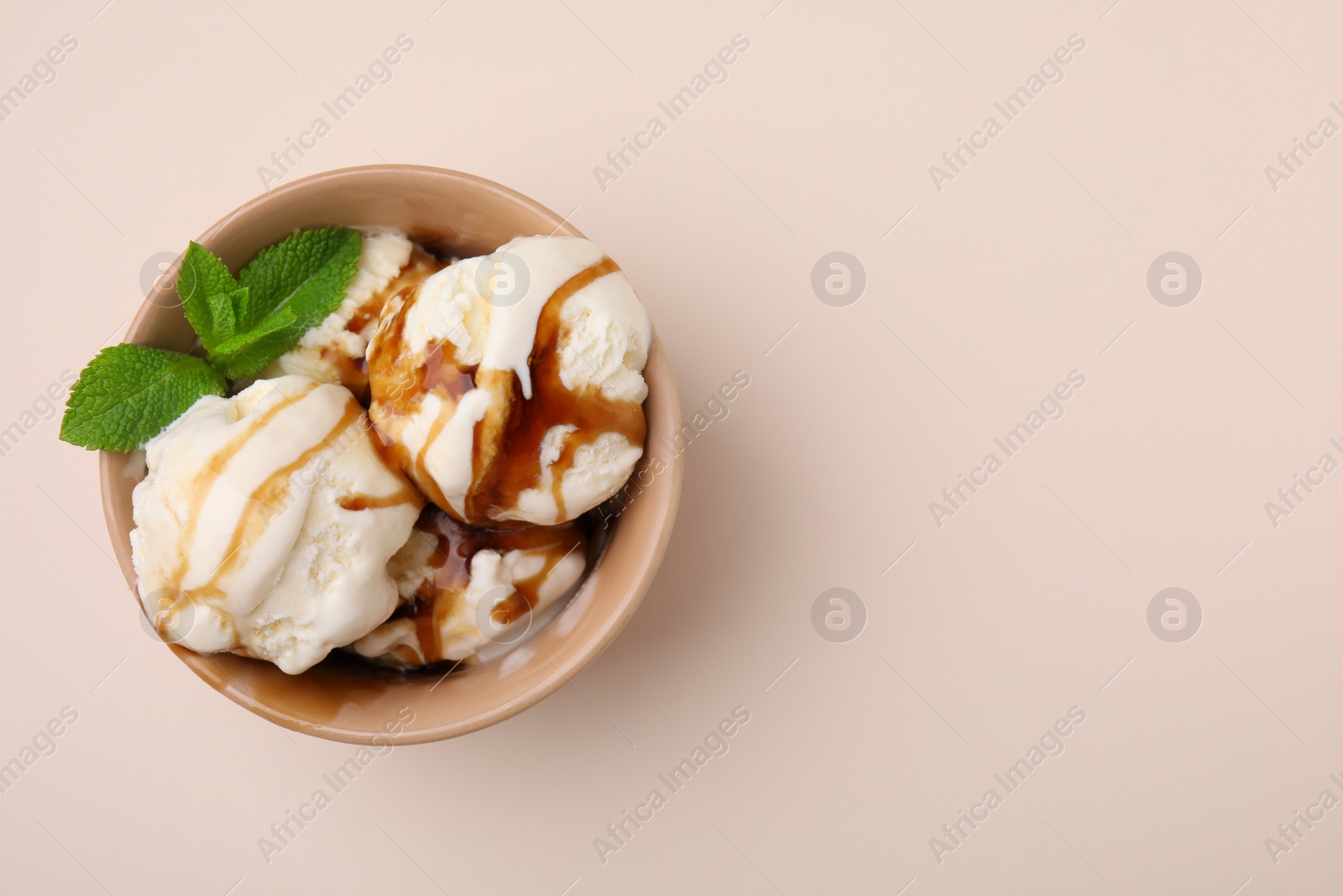 Photo of Scoops of ice cream with caramel sauce and mint leaves on beige table, top view. Space for text