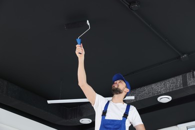 Photo of Worker in uniform painting ceiling with roller indoors