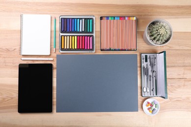 Layout with blank papers, soft pastels and other drawing supplies on wooden table at artist's workplace, top view. Space for design