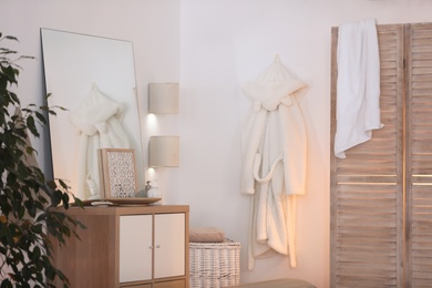 Photo of Stylish room interior with folding screen, wooden cabinet and mirror