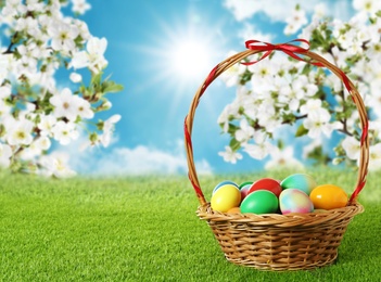 Image of Wicker basket with Easter eggs on green grass outdoors, space for text