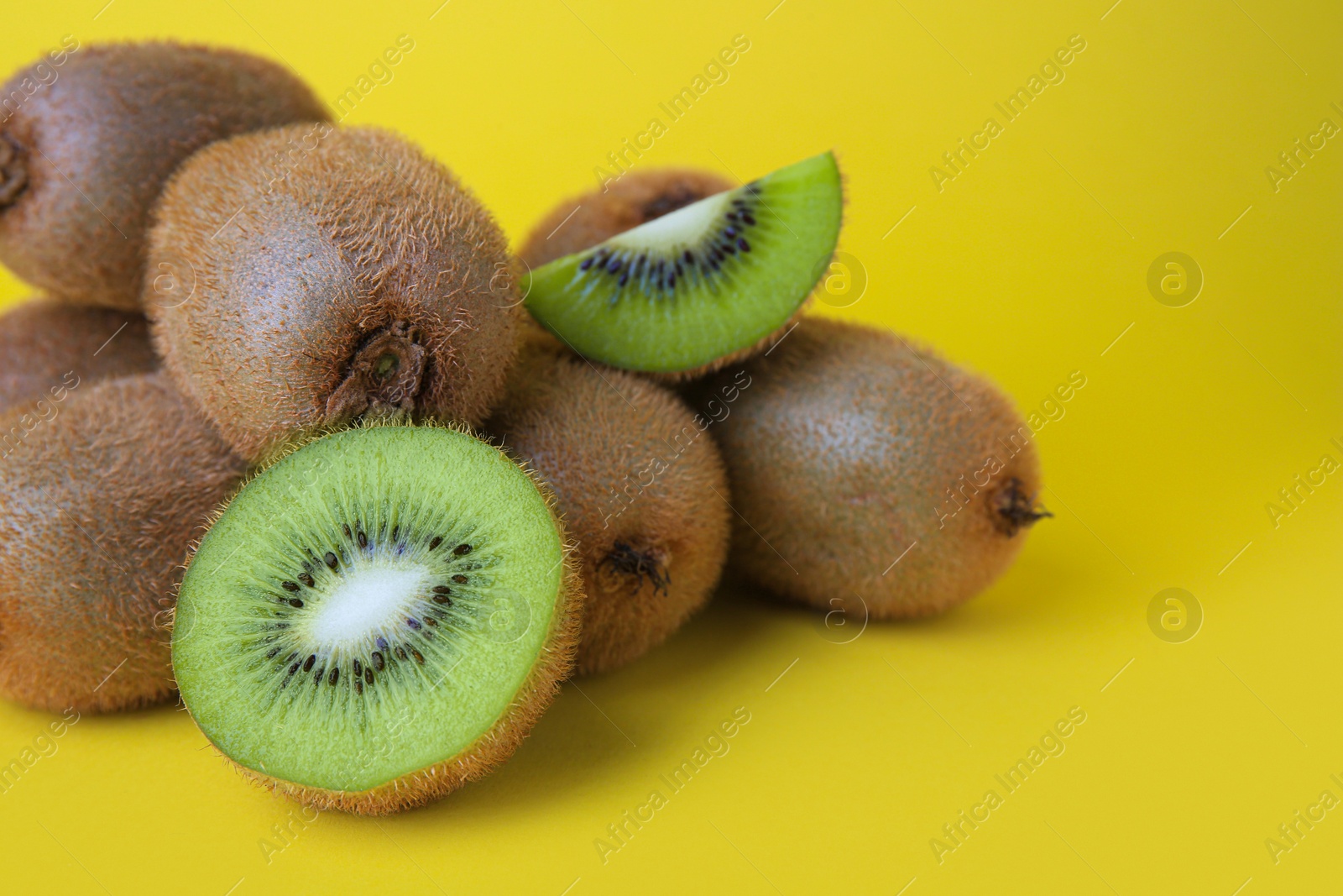 Photo of Heap of whole and cut fresh kiwis on yellow background, closeup. Space for text