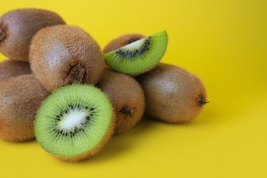 Photo of Heap of whole and cut fresh kiwis on yellow background, closeup. Space for text