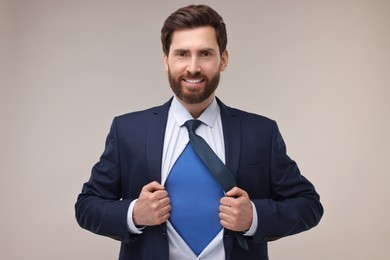 Happy businessman wearing superhero costume under suit on beige background