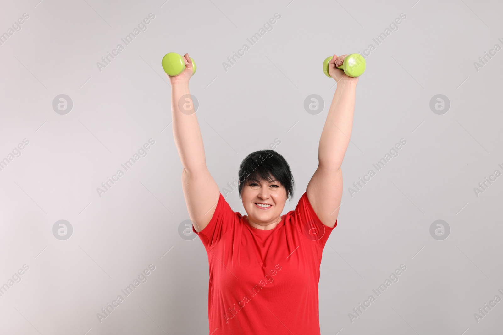 Photo of Happy overweight mature woman doing exercise with dumbbells on grey background