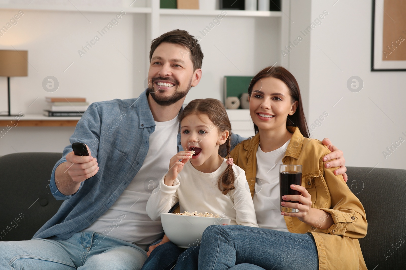 Photo of Happy family watching movie at home. Father changing TV channels with remote control