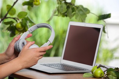 Photo of Woman holding headphones at wooden table with laptop, closeup