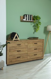 Photo of New wooden chest of drawers, plants and lamp near green wall in stylish room