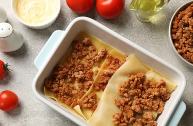 Cooking lasagna. Pasta sheets, minced meat in baking tray and products on light textured table, flat lay