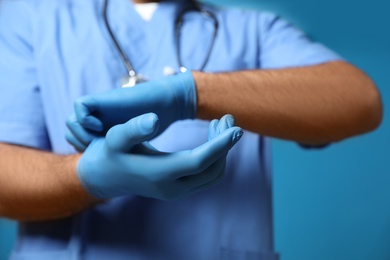 Photo of Doctor putting on medical gloves against blue background, closeup