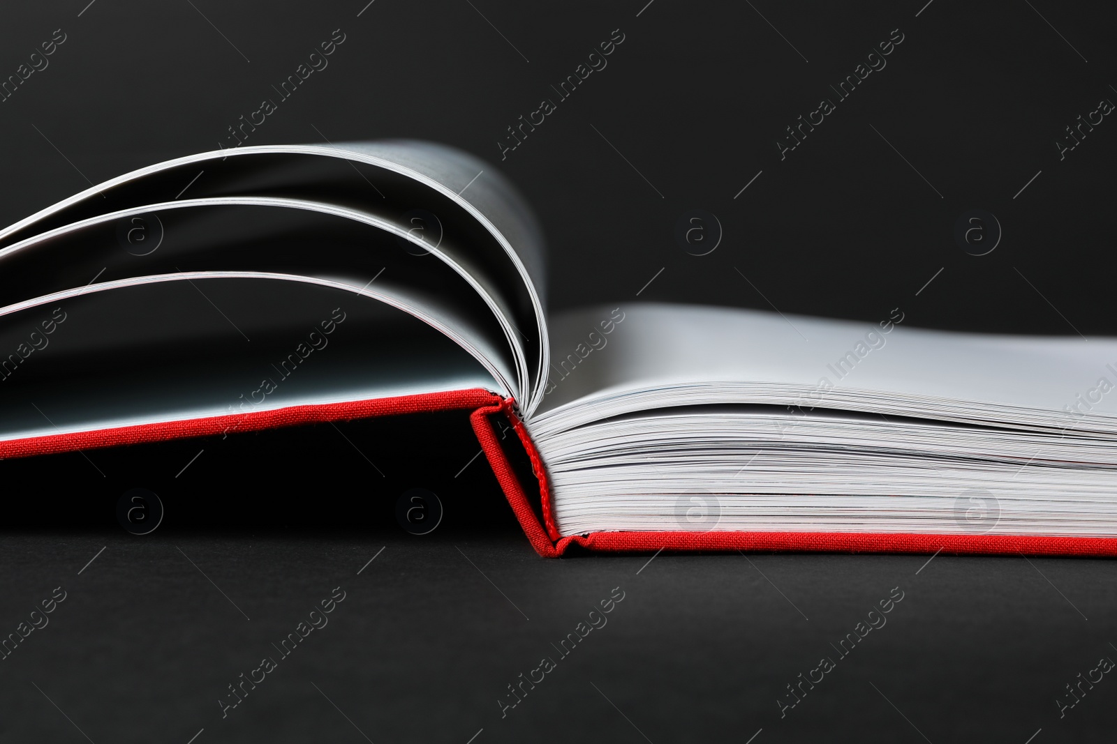 Photo of Open book with red cover on black background, closeup view