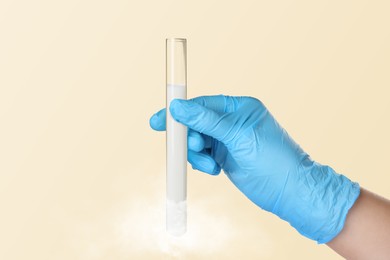 Cryopreservation. Laboratory assistant holding test tube with sperm on beige background, closeup. Frost effect