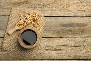 Photo of Soy sauce in bowl and soybeans on wooden table, flat lay. Space for text