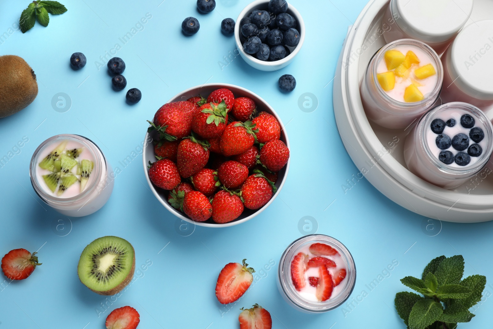 Photo of Tasty yogurt in glass jars and ingredients on light blue background, flat lay