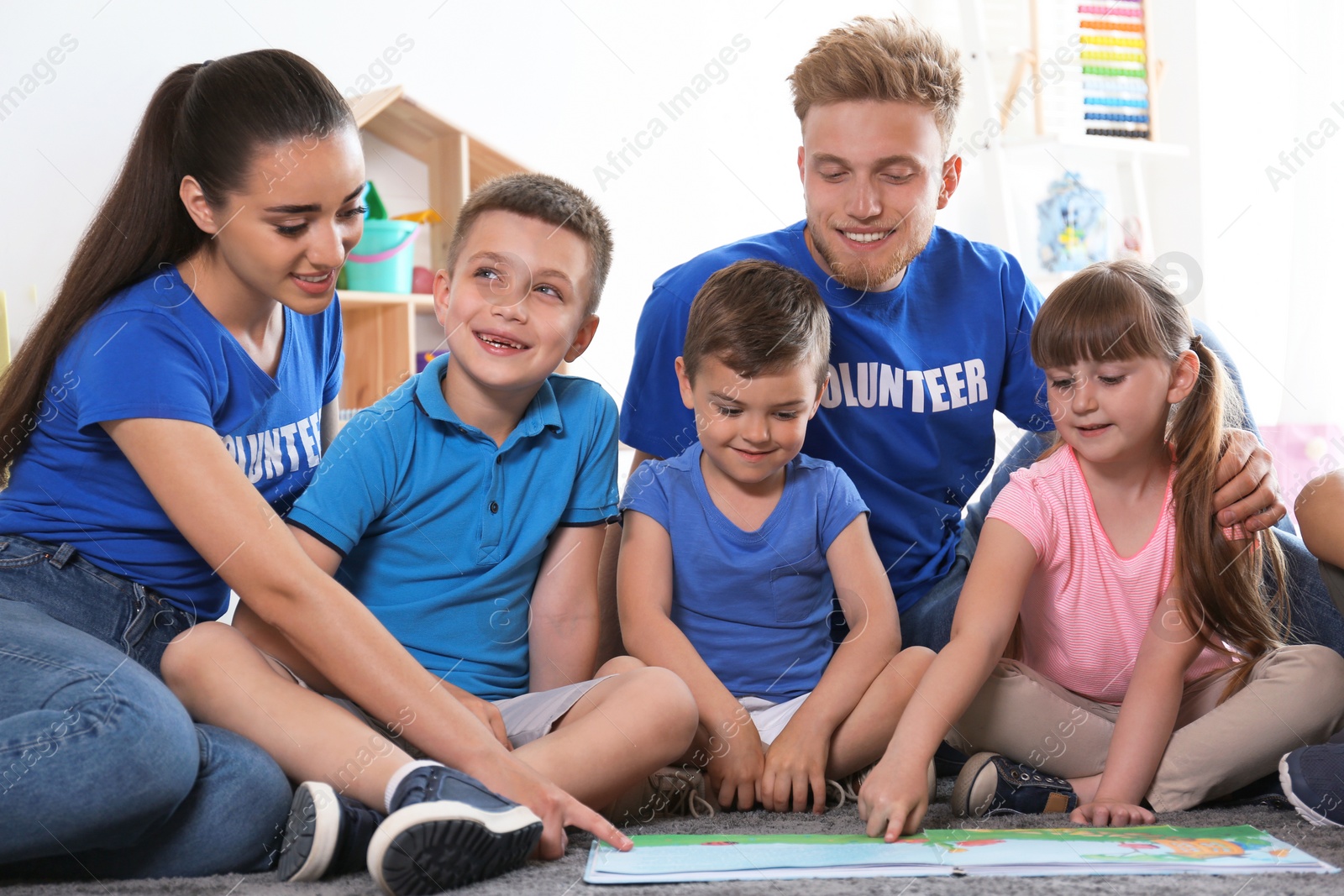 Photo of Young volunteers reading book with children on floor indoors