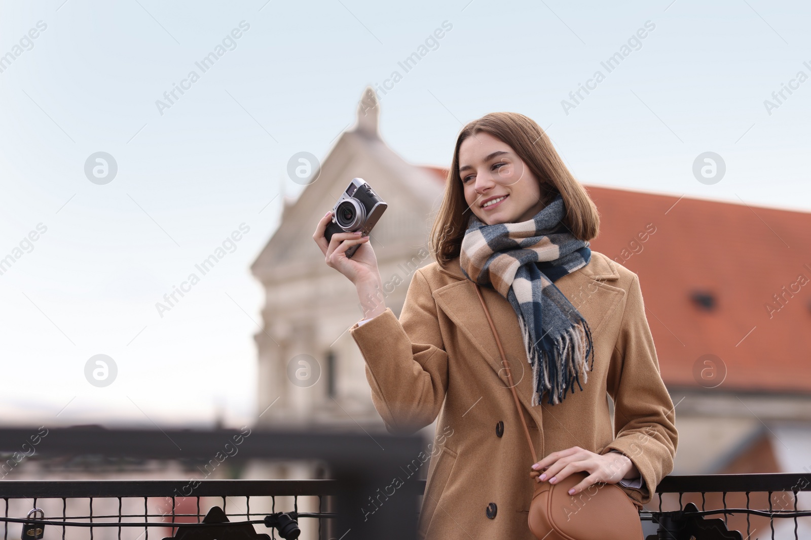 Photo of Beautiful woman in warm scarf taking picture with vintage camera outdoors, space for text