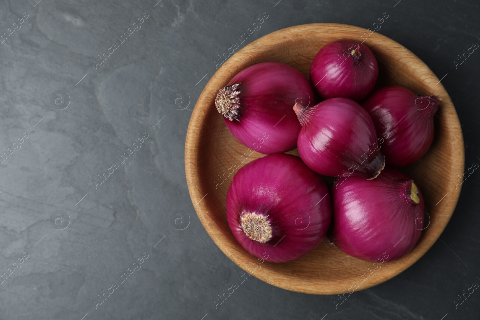 Photo of Ripe red onion bulbs in wooden bowl on black table, top view. Space for text