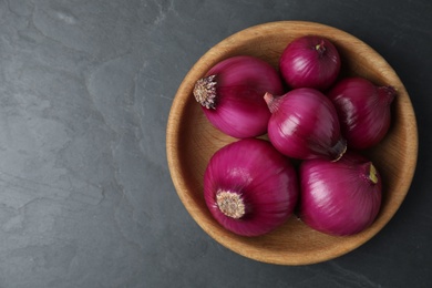 Ripe red onion bulbs in wooden bowl on black table, top view. Space for text