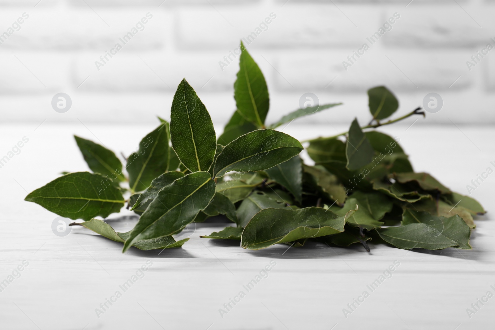 Photo of Fresh green bay leaves on white wooden table, closeup