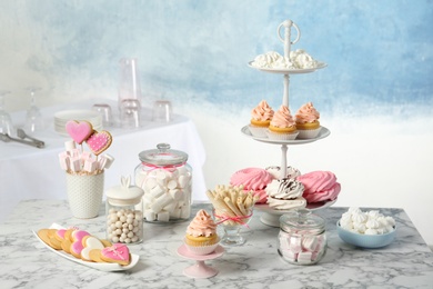 Candy bar with different sweets on white marble table against color background