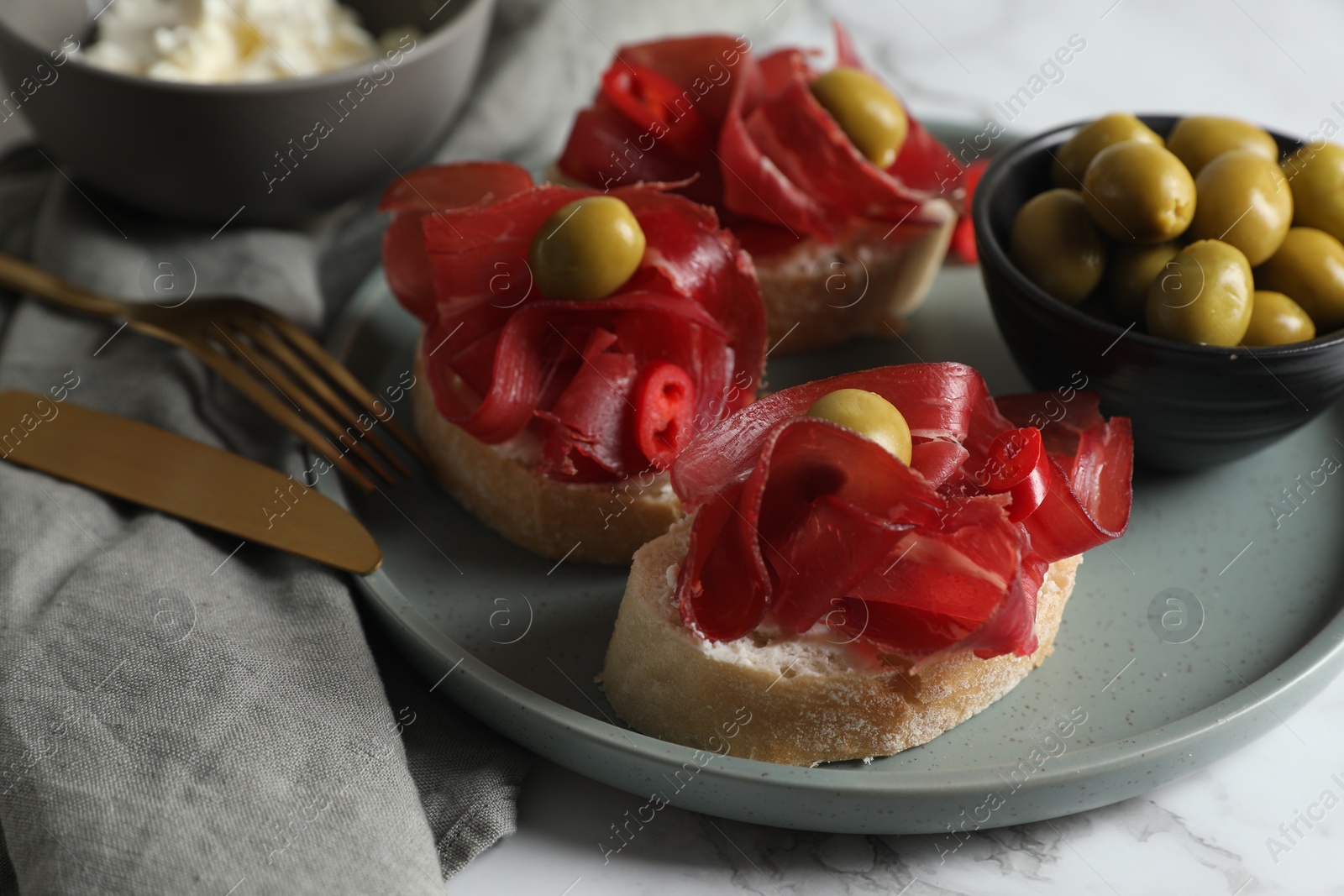 Photo of Delicious sandwiches with bresaola, cream cheese and olives served on white marble table, closeup