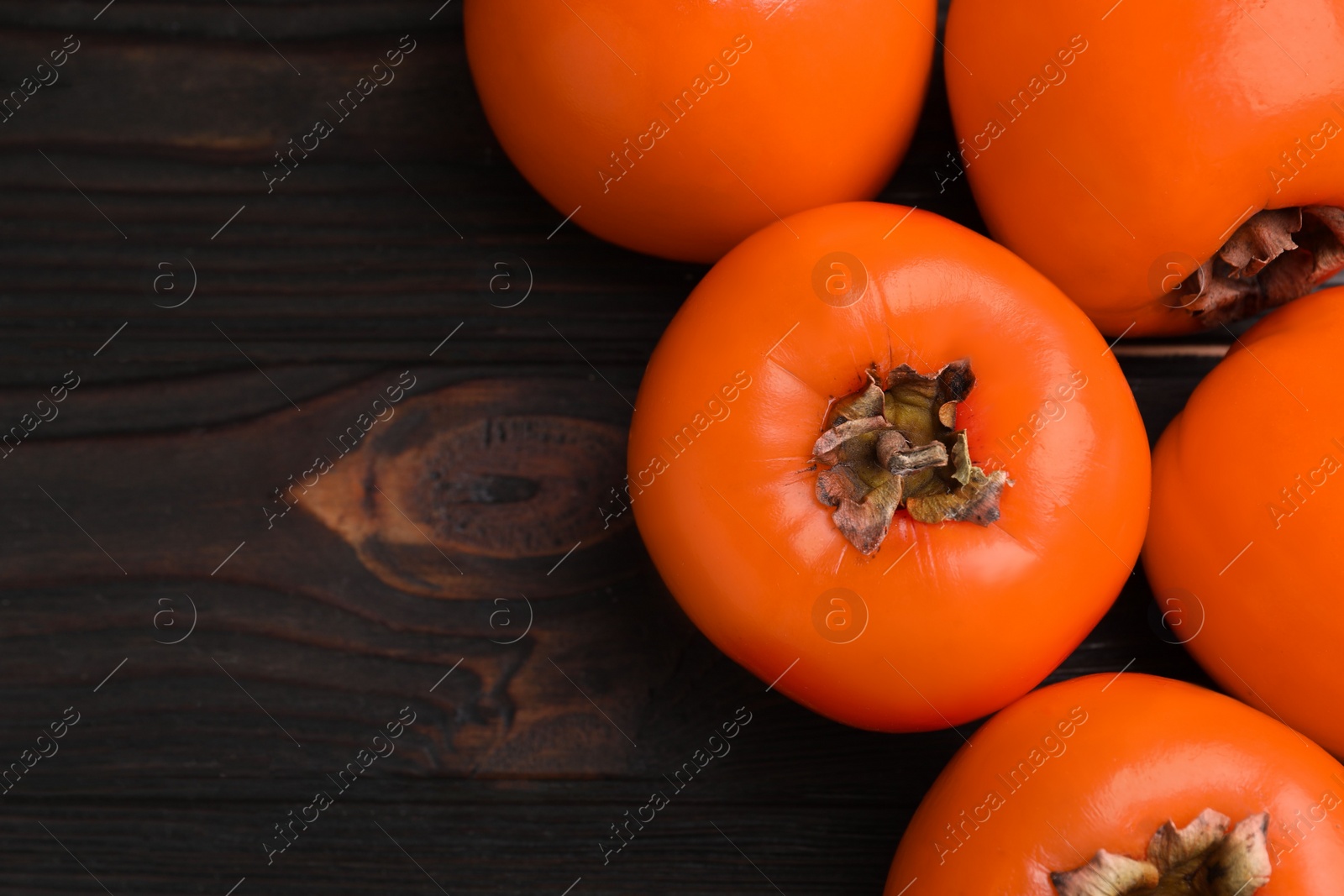 Photo of Delicious ripe persimmons on dark wooden table, top view. Space for text