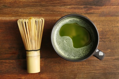 Cup of fresh matcha tea and chasen on wooden background, top view