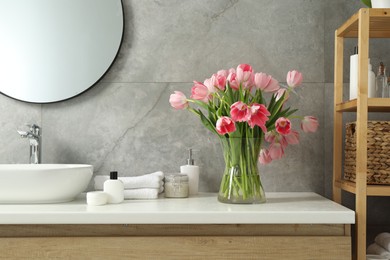 Vase with beautiful pink tulips and toiletries near sink in bathroom