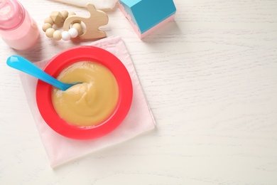 Flat lay composition with bowl of healthy baby food on white wooden table. Space for text