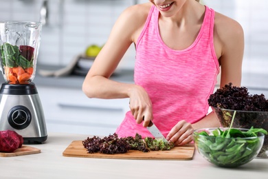 Photo of Young woman preparing tasty healthy smoothie at table in kitchen
