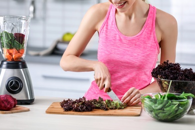 Young woman preparing tasty healthy smoothie at table in kitchen