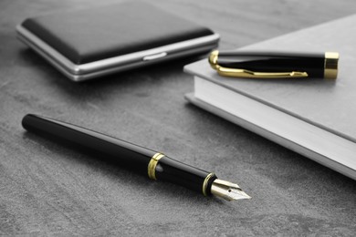 Photo of Stylish black fountain pen, notebook and cigarette case on grey textured table, closeup
