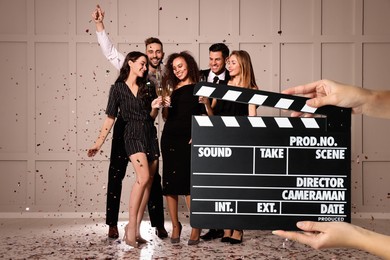 Image of Shooting movie. Second assistant camera holding clapperboard in front of happy friends celebrating holiday (actors) at film set
