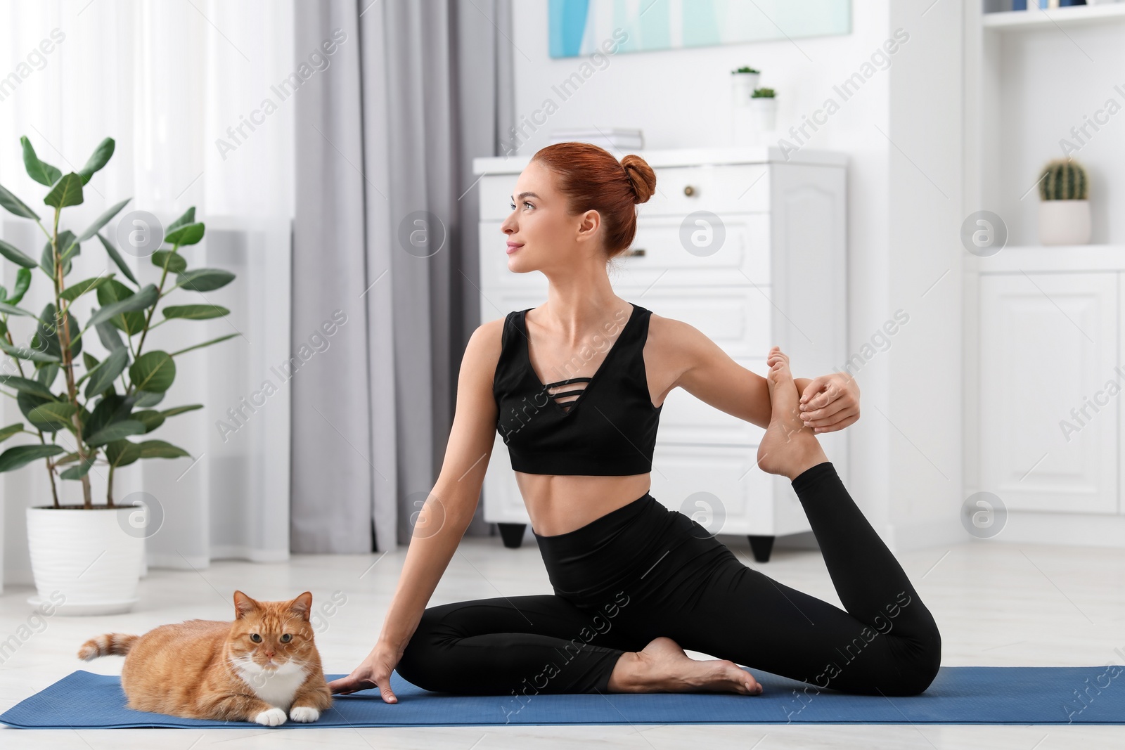 Photo of Beautiful woman with cute red cat practicing yoga on mat at home