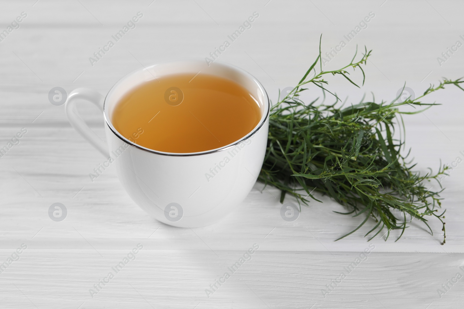 Photo of Aromatic herbal tea and fresh tarragon sprigs on white wooden table