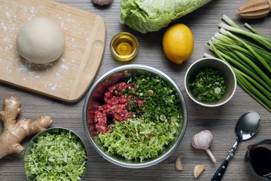 Photo of Bowl with gyoza filling, raw dough and ingredients on wooden table, flat lay