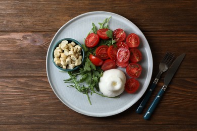 Photo of Delicious burrata cheese with tomatoes and arugula served on wooden table, top view